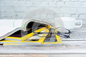 Stack magazines with glasses on wooden table.