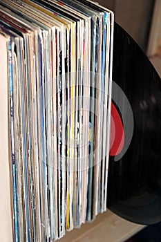 Stack of many vinyl records in old color covers on wooden shelf side view