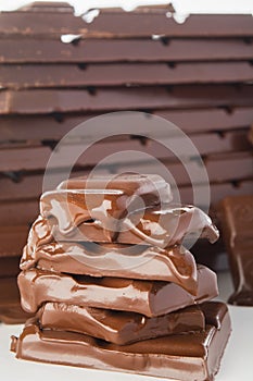 Stack of melting chocolate`s pieces with big stack of chocolate on background