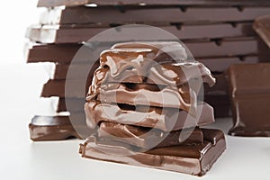 Stack of melting chocolate`s pieces with big stack of chocolate on background