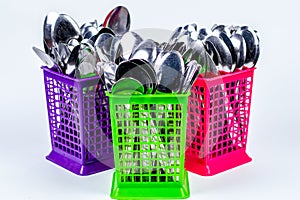 stack of metal spoons in colorful plastic baskets isolated on white background