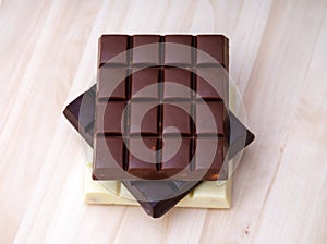 Stack of milk chocolate, dark chocolate and white chocolate bars on a wooden background