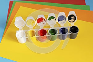 Stack of multi-colored paper and paint for drawing on a blue background.