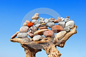 Stack of multicolored balanced stones on an old wooden snags, on a blue sky background