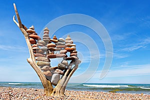 Stack of multicolored balanced stones on an old wooden snags, on a blue sky and sea background