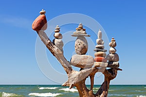 Stack of multicolored balanced stones on an old wooden snags, on a blue sky and sea background