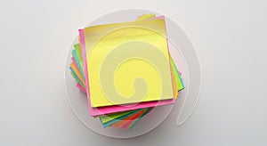 A stack of multicolored sticky notes is arranged in a neat pile. The top note is bright photo