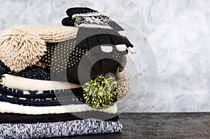 A stack of neatly folded knitted winter scarves, hats with pompons and gloves on gray background. Season of warm clothes