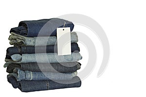 A stack of new jeans with white paper tag mockup and copy space isolated on white