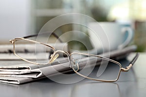 Stack of newspapers and glasses on grey table indoors, closeup