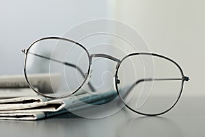 Stack of newspapers and glasses on grey table indoors, closeup