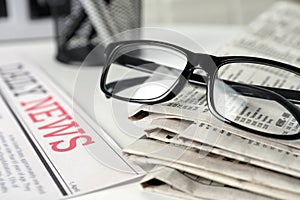 Stack of newspapers and glasses on white table, closeup