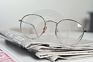 Stack of newspapers and glasses on white table indoors, closeup