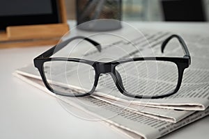 Stack of newspapers and glasses on white table indoors, closeup