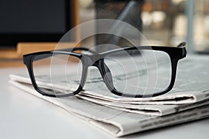 Stack of newspapers and glasses on white table indoors, closeup