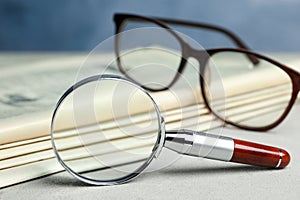 Stack of newspapers, magnifier and glasses on table. Search