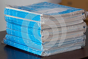 Stack of Notebooks. A pack of blue school notebooks in cellophane on the table in a classroom. Stack of exercise books. Ruled