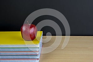 Stack of notebooks with red apple and clean blackboard