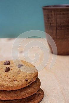 Stack oatmeal cookies with chocolate crisps and brown ceramic glass of milk on wooden table