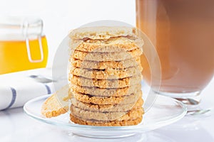 A stack of oatmeal cookies in a glass plate. Coffee in an Irish coffee glass, orange jam in a jar with a yoke. Linen napkin with a