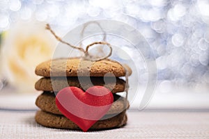 Stack of oatmeal cookies and heart, blurred background. Gifts for loved ones. The photo