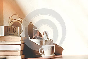 Stack old books with a cup of freshly coffee, vintage alarm clock, wooden calendar, on table in sunlight morning