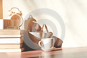 Stack old books with a cup of freshly coffee, vintage alarm clockon, wooden calendar, on table in sunlight morning, Start up