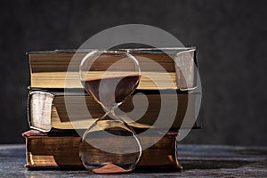 A stack of old books and an hourglass. The concept of time and knowledge