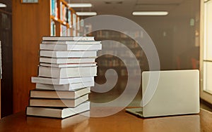 Stack of old books and laptop computer on desk in library background. Educational technology concept