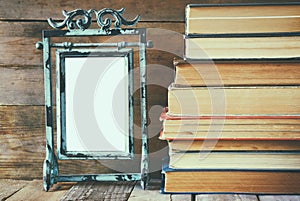 Stack of old books next to vintage blank frame wooden table. vintage filtered image