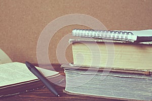 Stack of old books, notebook, opened book with pen on wooden tab