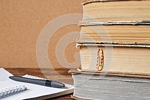 Stack of old books, notebook with pen on wooden table