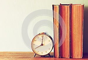 Stack of old books and old clock over wooden table . filtered image