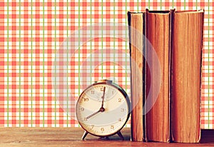 Stack of old books and old clock over wooden table and retro style wallpaper