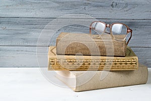 Stack of old books and reading glasses on wooden background