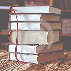A stack of old books on table against background of bookshelf in library. Conceptual background on education, literature photo