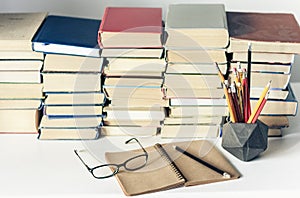 Stack of old books, textbook, notebook, glasses and pencils on white table in office background for education concept