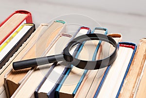 Stack of old hardback books with magnifying glass. Search for relevant and necessary information in a large number of sources