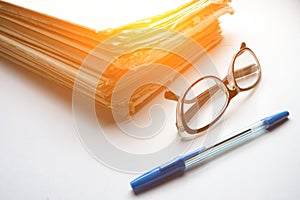 Stack of old newspapers, ballpoint pen and reading glasses on a white background with bright sunlight from window