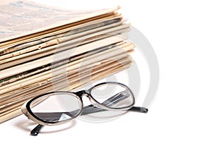 Stack of old newspapers and reading glasses on a white background