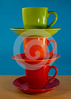 Stack of orange, green, red cups in saucers stand on a wooden table on a blue background