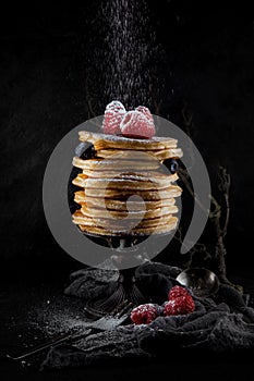 A stack of pancakes decorated with berries and powdered sugar, rustic studio shot