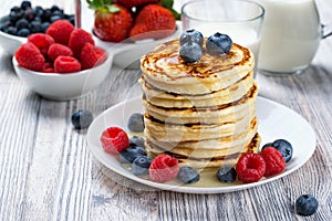 Stack of pancakes with fresh blueberry and raspberry, poured with honey. Milk and fresh berries, healthy breakfast concept