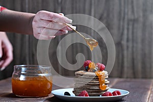 A stack of pancakes with fresh raspberries and blueberries topped with jam on a light plate on a wooden background