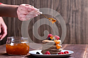 A stack of pancakes with fresh raspberries and blueberries topped with jam on a light plate on a wooden background