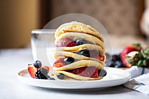 Stack of pancakes with fruits and berries, glass of milk on a gray background