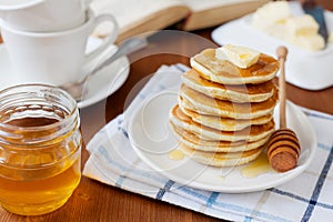 Stack of pancakes with honey syrup, butter and strawberry in a white plate