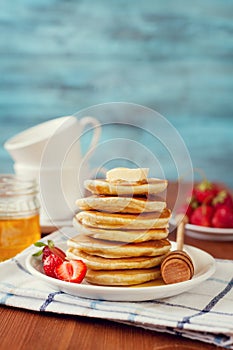 Stack of pancakes with honey syrup, butter and strawberry in a white plate
