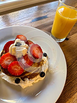 Stack of pancakes with strawberries, blueberries, bananas, and cream with juice