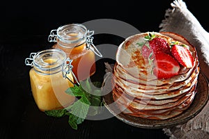 A stack of pancakes with strawberries and mint . Jars of honey on the table. Photo on a black background. Copy of the space.